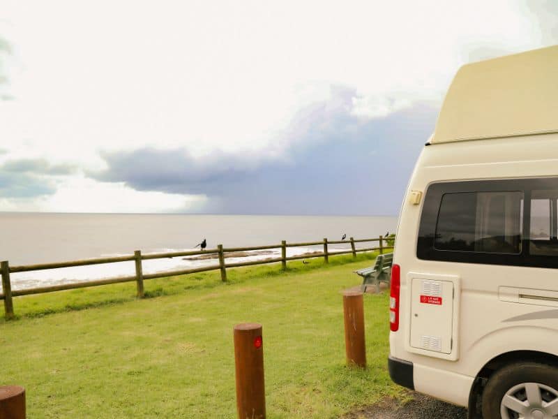 Back part of a parked campervan on a green spot overlooking the ocean.
